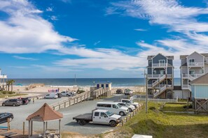 A beachfront parking area with multiple vehicles, a gazebo, and a row of multi-story buildings with balconies. - Mermaid Avenue Oceanview 4 Bedroom Home in Surf City – Perfect for the whole (Surf City)