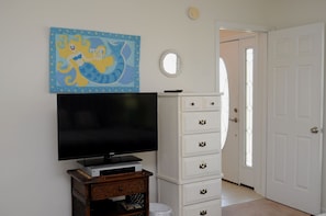 A room with a flat-screen TV on a wooden stand, a white dresser with multiple drawers, and a wall-mounted mirror.