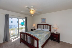 A bedroom with a bed, two bedside tables, a ceiling fan, a window with curtains, and a picture on the wall. - Mermaid Avenue Oceanview 4 Bedroom Home in Surf City – Perfect for the whole (Surf City)