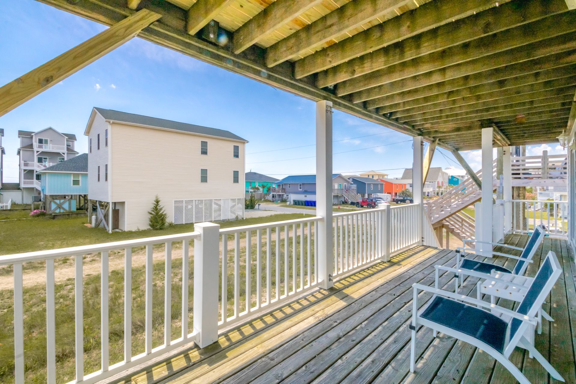 A wooden deck with white railings, overlooking a residential area with houses and a clear sky.