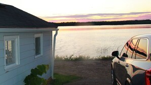 Una casa con puerta de garaje y un coche aparcado al lado, con vistas a un lago tranquilo bajo un cielo al atardecer.