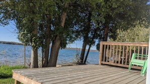 Un muelle de madera con una silla verde, con vista a un lago bordeado de árboles.