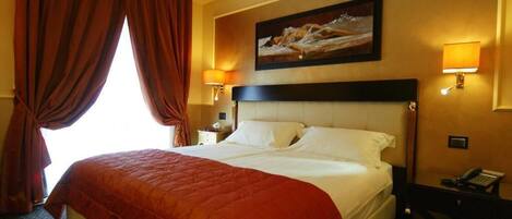 A hotel room with a large bed, two bedside lamps, a desk with a telephone, and a painting on the wall.