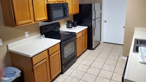Una cocina compacta con armarios de madera, una estufa negra, un microondas, un refrigerador y una encimera blanca.