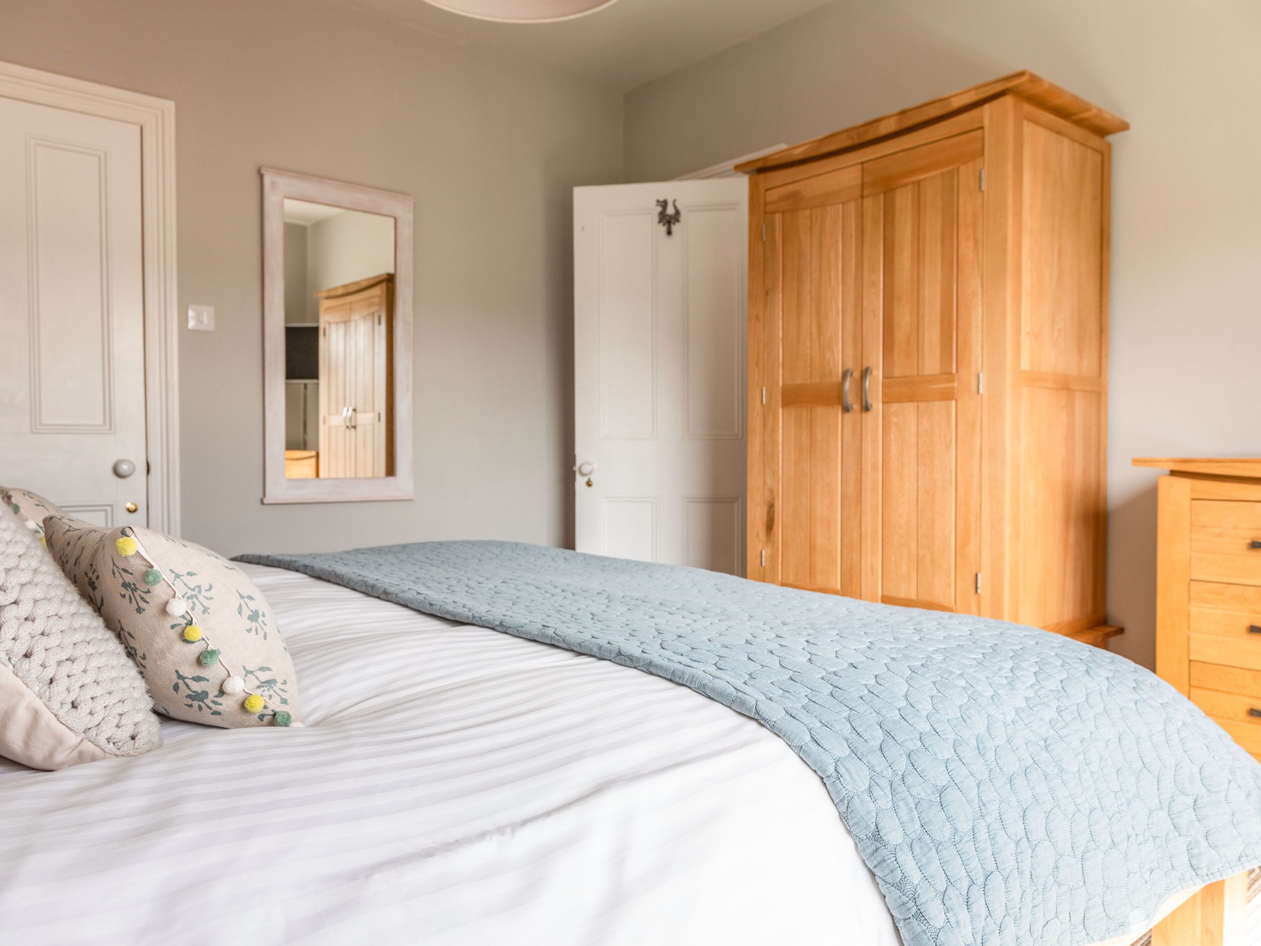 A bedroom with a bed, a wooden wardrobe, a mirror, and a door.