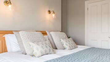 A neatly made bed with a blue quilt, white pillows, and a wooden headboard. Two wall-mounted light fixtures are visible.