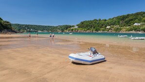 A beach with a small inflatable boat on the sand, a clear blue sky, and a few people in the distance. - Higher Cliftonville (Dorking)
