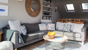 A modern living room with a grey sofa, a round coffee table, and a wooden-framed mirror. There are bookshelves and a skylight above the sofa. - Higher Cliftonville (Dorking)