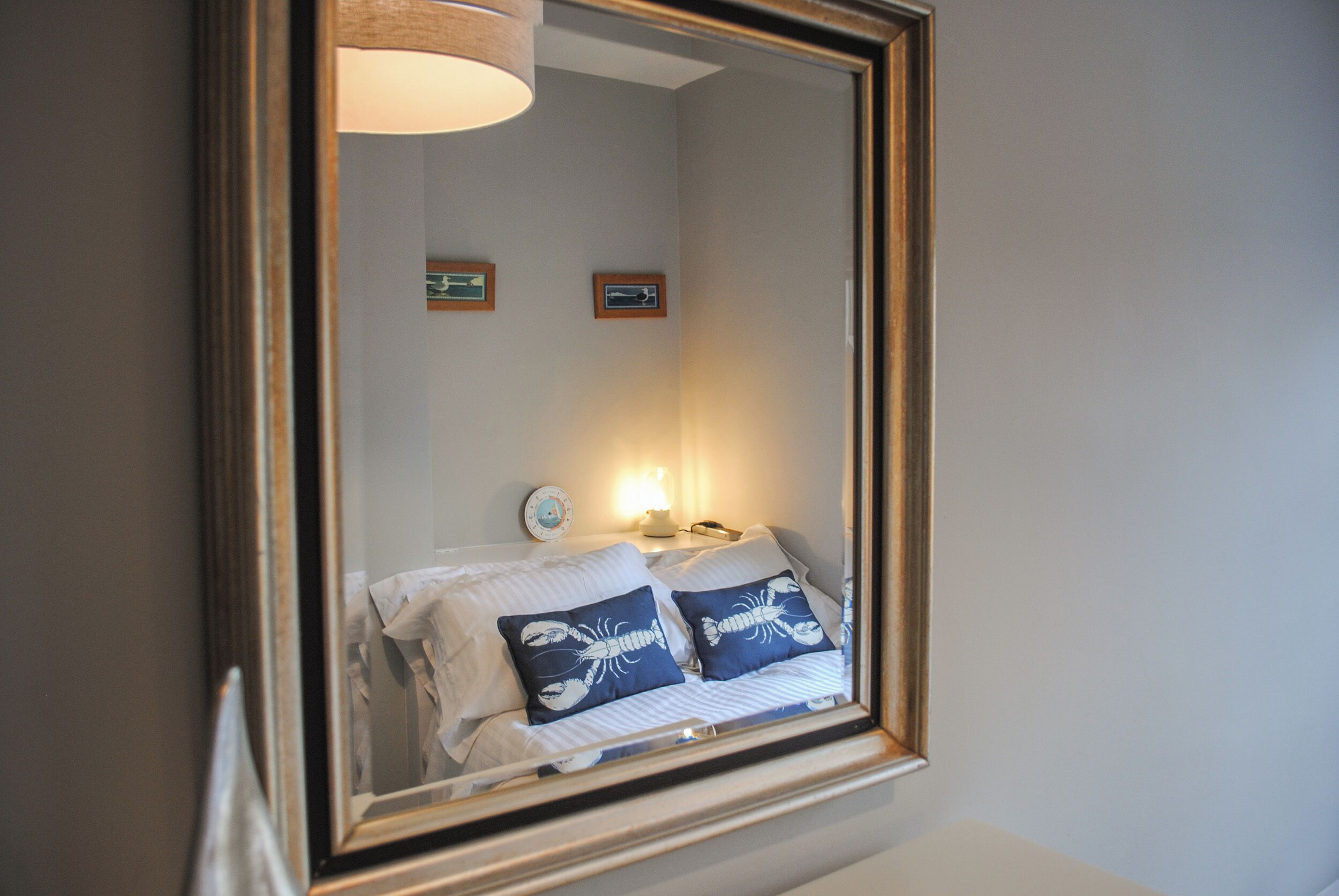 A bedroom with a bed, pillows, a nightstand, and a wall-mounted mirror.