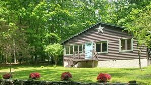 Eine Blockhütte mit Veranda, umgeben von einer Steinmauer und roten blühenden Büschen.