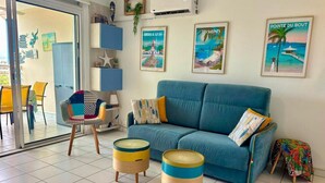 A living room with a blue sofa, two round side tables, a chair, and a glass door leading to a balcony. - Martinique!  Beautiful, fully renovated studio with sea view (ANSE MITAN - LES 3 ILETS)