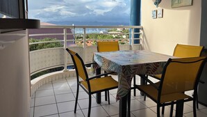 A balcony with a table and chairs, a view of the sea, and a building in the background. - Martinique!  Beautiful, fully renovated studio with sea view (ANSE MITAN - LES 3 ILETS)