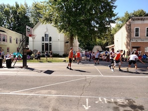 An outdoor basketball court with a hoop, surrounded by spectators and buildings.