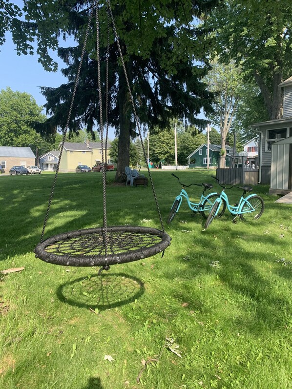 A grassy yard with a swing set, a bicycle, and a tree.
