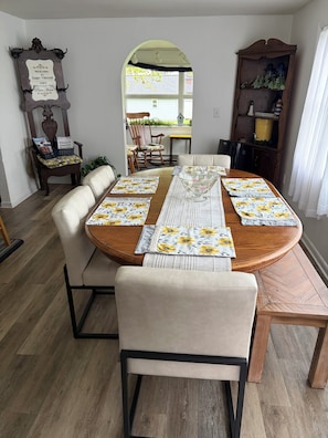A dining area with a round wooden table, beige upholstered chairs, and floral tablecloths.