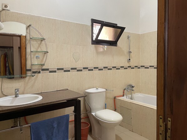 A bathroom with two sinks, a toilet, a bathtub, a mirror, and a showerhead. - Sérénité double room (Ziguinchor)