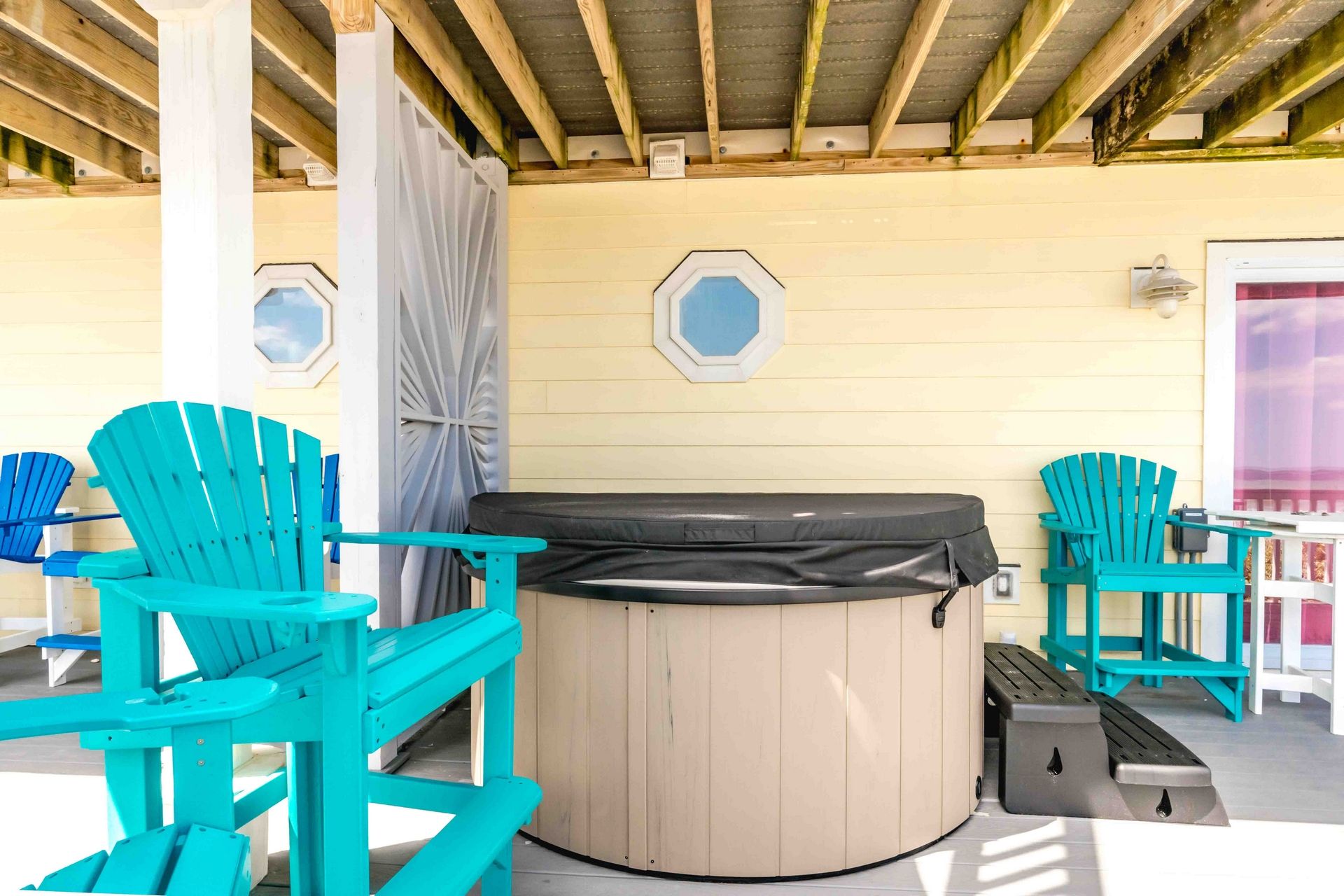 Un espacio de estar al aire libre techado con jacuzzi, terraza de madera y dos sillas Adirondack.