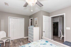 A bedroom with a bed, a chair, a dresser, a wardrobe, and a ceiling fan.