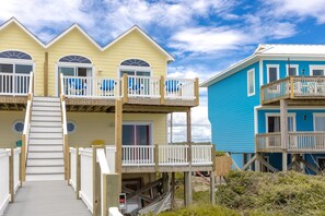 Une propriété située en bord de mer, avec un bâtiment à deux étages doté d’une terrasse en bois et d’un escalier menant à un balcon.