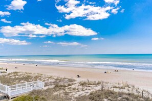 Une plage bordée d’une clôture blanche, avec des dunes de sable et un ciel bleu dégagé.