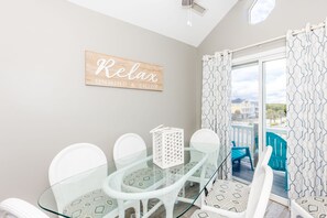 Een balkon met een glazen tafel en stoelen, een bord met de tekst 'Relax' en gordijnen met een patroon.