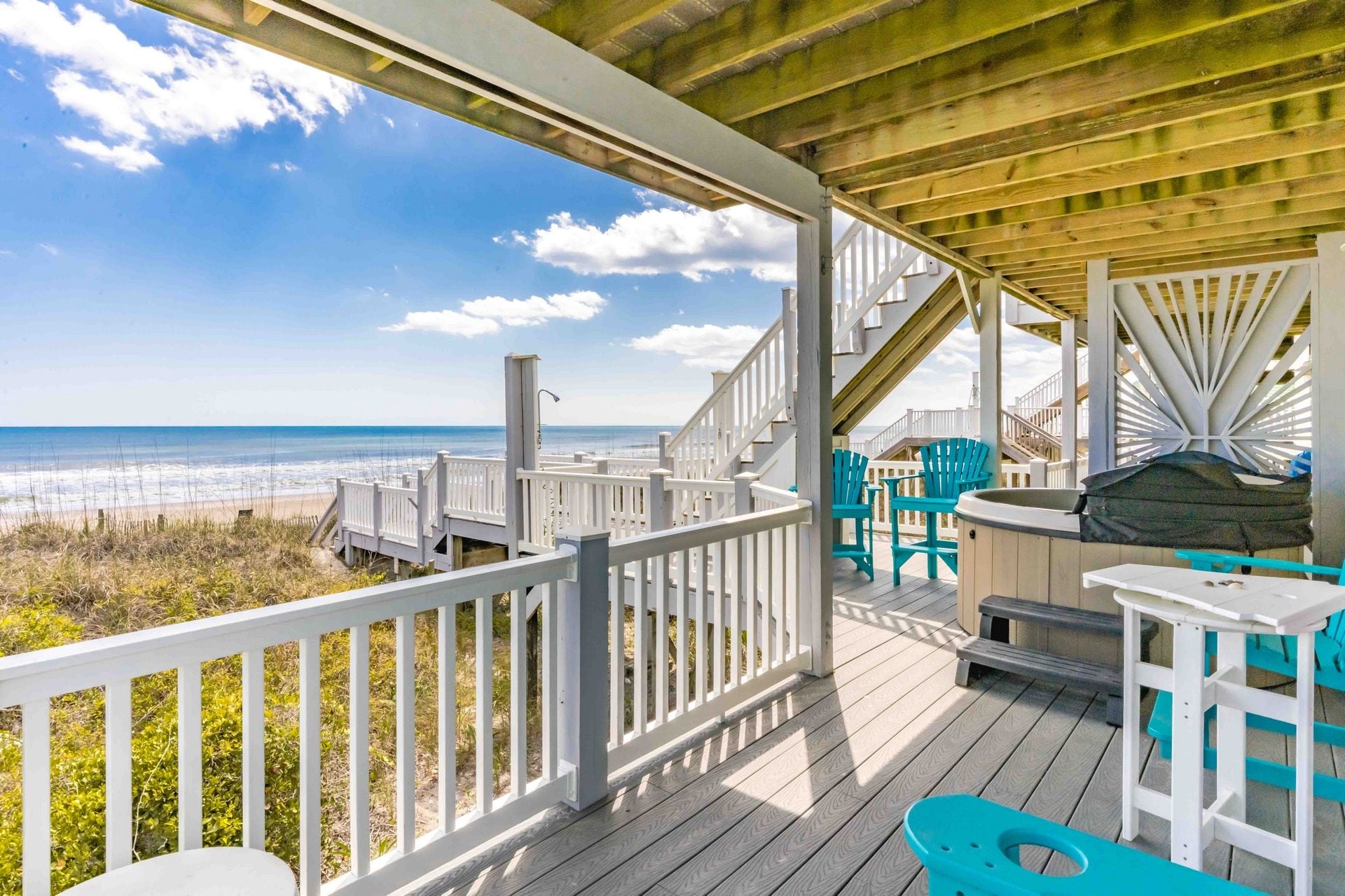 A wooden deck with a view of the beach, outdoor seating, and a hot tub.