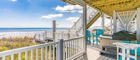 A wooden deck with a view of the beach, outdoor seating, and a hot tub.