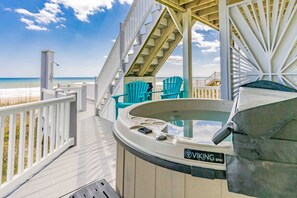 Een houten terras met een jacuzzi, stoelen en een trap naar uitzicht op het strand.