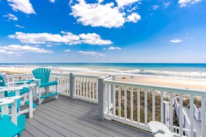 A wooden deck with chairs and a toilet, overlooking a beach with waves and a clear sky.