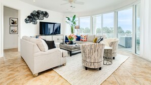 Un salon spacieux doté d’un grand téléviseur, de sièges confortables et offrant une vue sur l’extérieur.