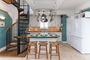 A kitchen with a central island, a white refrigerator, and a wooden staircase. - Tower Four - Oceanfront Historic Missile Tower - 3 BR / 2.5 BATH (Surf City)