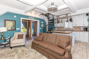 A living room with a sofa, a lamp, a rug, and a staircase leading to a kitchen with white cabinets and a window.