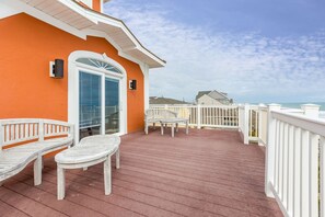 A wooden deck with a white railing, a glass door, and two white chairs.
