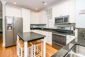 A modern kitchen with white cabinets, stainless steel appliances, a black countertop, and a bar stool. - Vitamin Sea - Oceanfront, 5 BR Home in Surf City - Elevator! (Surf City)