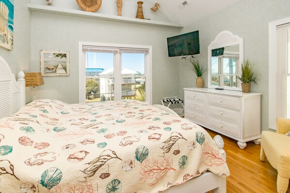 A bedroom with a bed, dresser, TV, and large windows.