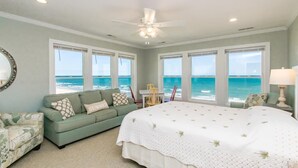 A bedroom with a large bed, a green sofa, a chair, and a table. There are large windows with a view of the ocean. - Vitamin Sea - Oceanfront, 5 BR Home in Surf City - Elevator! (Surf City)