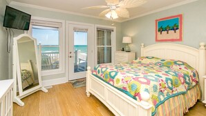 A bedroom with a bed, a ceiling fan, a television, a dresser, a nightstand, a window with a view of the ocean, and a door leading to a balcony. - Vitamin Sea - Oceanfront, 5 BR Home in Surf City - Elevator! (Surf City)