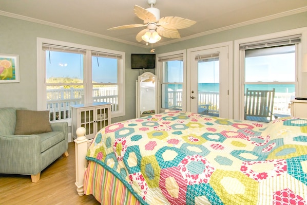 A bedroom with a large bed, a chair, a ceiling fan, and a view of the beach through the windows. - Vitamin Sea - Oceanfront, 5 BR Home in Surf City - Elevator! (Surf City)