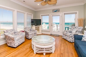 A living room with a television, two patterned armchairs, a round wicker coffee table, and a sofa.