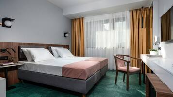 Ein Hotelzimmer mit Bett, Schreibtisch, Stuhl, Fernseher und einem Fenster mit Vorhängen.
