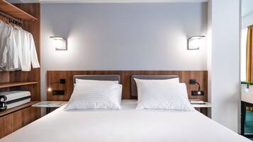 A modern hotel room with a large bed, wooden headboard, two bedside tables with lamps, a wardrobe, and a small table with a book.