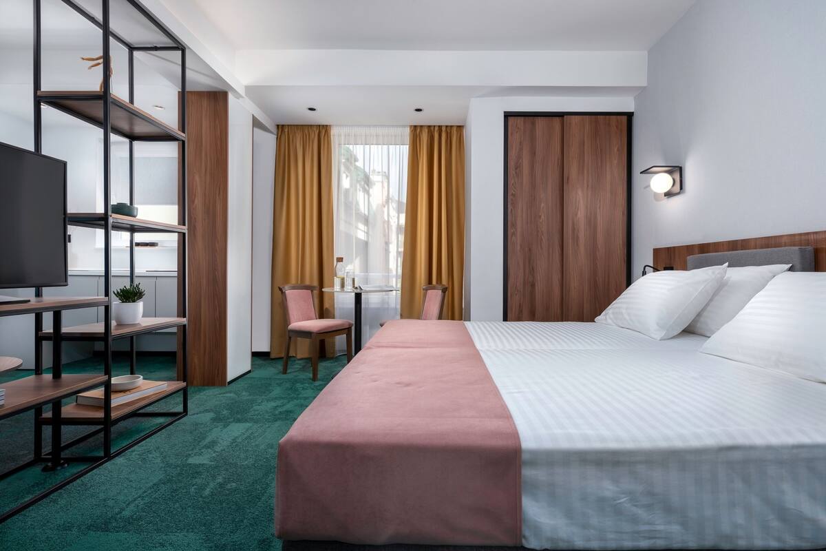 Habitación de hotel con cama, escritorio, silla, televisor y estantería.