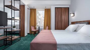 A hotel room with a bed, a desk, a chair, a TV, and a bookshelf.