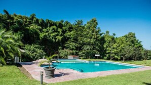 A rectangular swimming pool with a stone border, surrounded by a well-maintained lawn and dense greenery. - The Royal Solwezi Hotel (Solwezi)