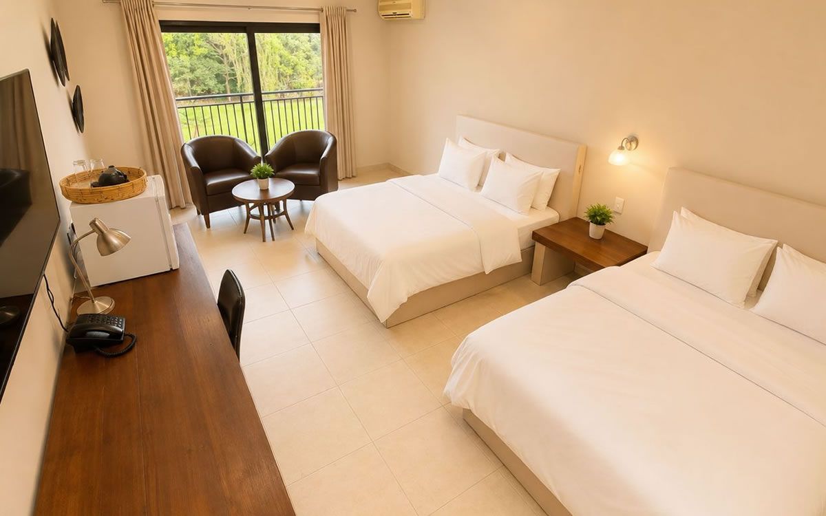 A hotel room with two beds, a desk with a lamp, a chair, a small table with a plant, and a balcony with a view.