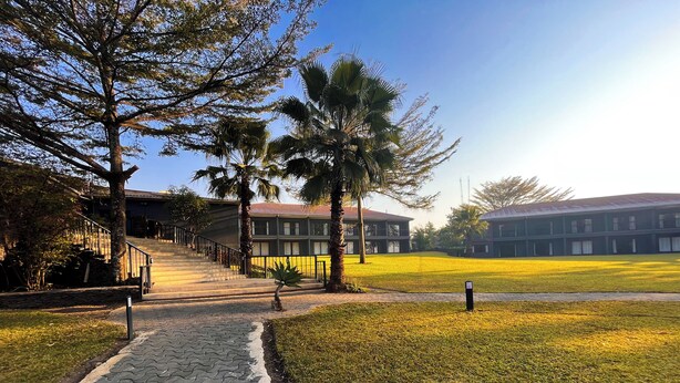 A paved pathway leading to a building with a staircase, surrounded by grass and trees. - The Royal Solwezi Hotel (Solwezi)
