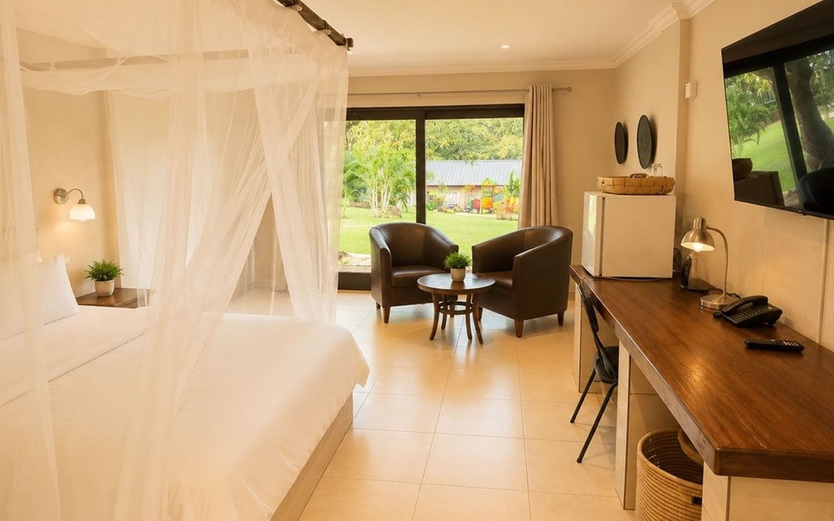 A hotel room with a bed, a desk, a chair, a small table, and a TV.