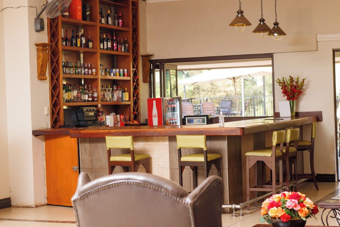 A bar area with a wooden counter, bar stools, a bookshelf with liquor bottles, and a view through the window.