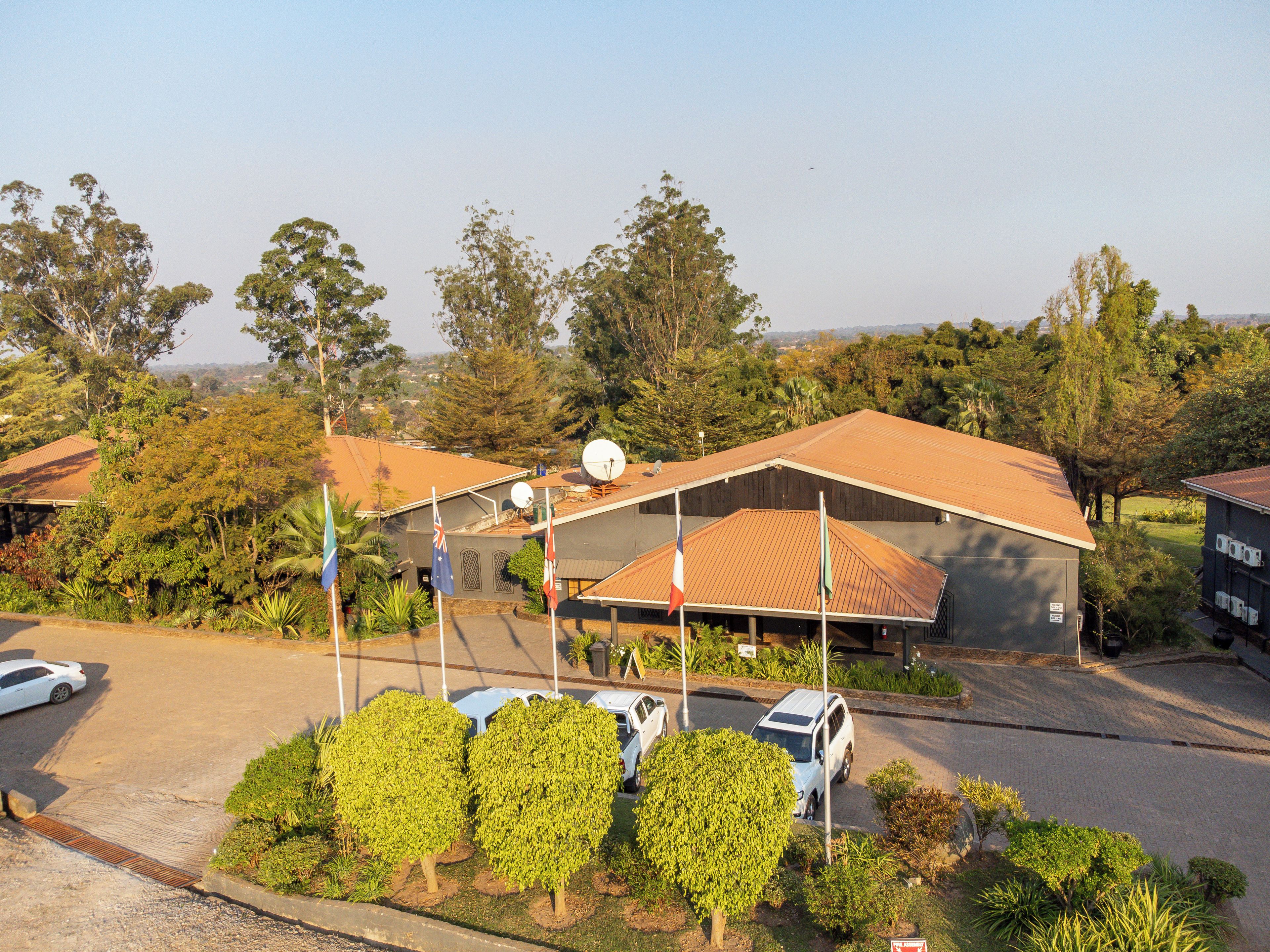 A building with a flat roof, surrounded by greenery and parked cars.