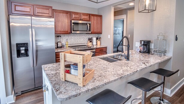 A modern kitchen with stainless steel appliances, wooden cabinets, granite countertops, and bar stools. - Lovely 3 BR Home Only 9 Minutes From Downtown (San Antonio)